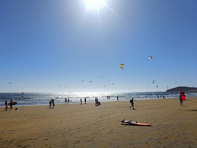 Strand mit vielen Windsurfern und Kitesurfern im Sonnenschein