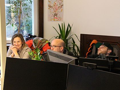 Drei Mitarbeiter, eine Frau und zwei Männer, sitzen an einem Schreibtisch und schauen sich etwas auf dem Bildschirm an.