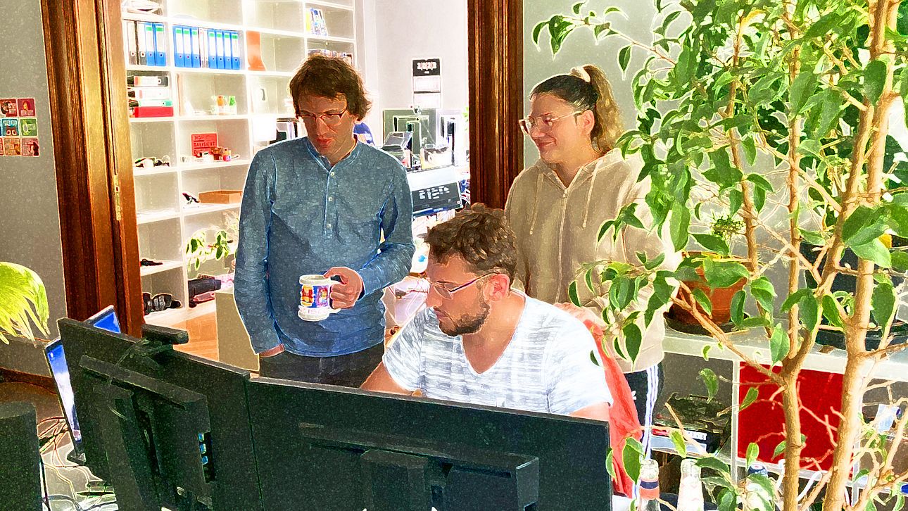 Drei werkraum-Mitarbeiter besprechen etwas direkt am Schreibtisch und schauen dabei auf den Monitor.
