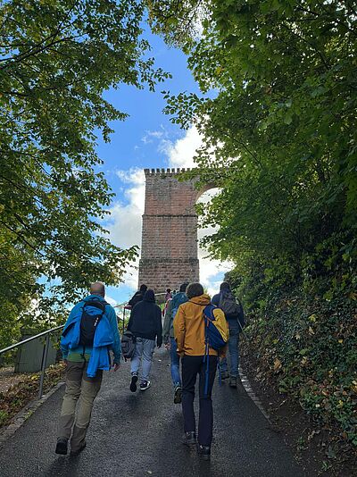Das Team wandert zur Burg Trifels hoch, man sieht sie von hinten, wie sie Richtung Eingangstor laufen